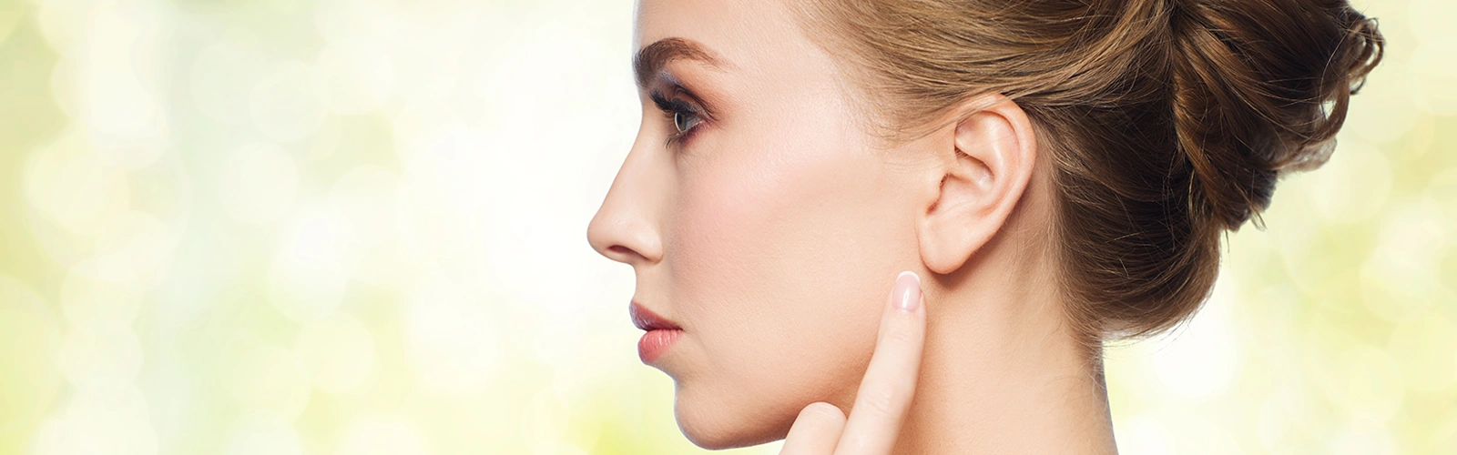Side profile of woman pointing to jawline showing natural facial contour after cosmetic surgery
